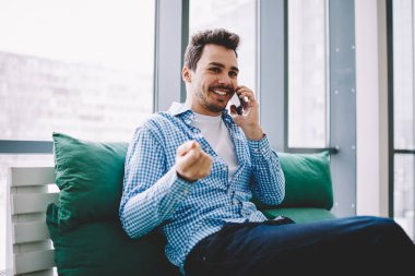 Mutlu gülümseyen erkek iletişim için arkadaşa arama ve rahat kanepede eğlence sırasında kapalı akıllı telefon konuşma yapmak için 4g kablosuz internet bağlantısı kullanarak toplantı için zaman tartışmak