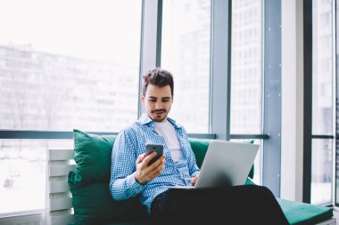 Pozitif hipster adam cep telefonu ve dizüstü bilgisayar cihazı ile bluetooth bağlantısı kullanarak uzaktan kapalı çalışırken bilgi paylaşımı, beyaz erkek cep telefonu uygulaması üzerinden gelen mesajı okuma