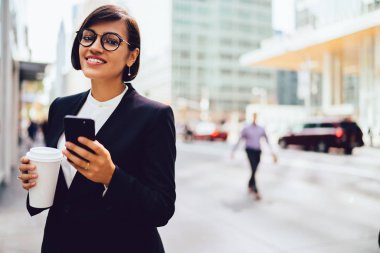 Optik gözlük neşeli esmer kurumsal patron yarım uzunlukta portre iş bölgesinde kahve molası için zaman zevk, modern akıllı telefon cihazı tutan resmi giyim mutlu gülümseyen kadın