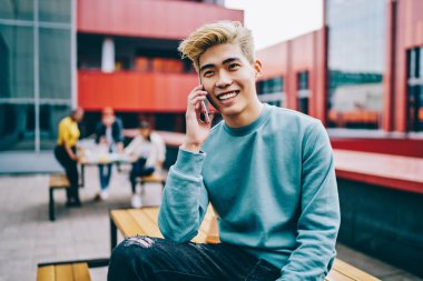 Açık havada gülümseyen ve konuşan neşeli Japon hippi. Şık giyinmiş Çinli genç adam cep telefonundan arıyor ve arkadaşlarıyla iletişim kuruyor.