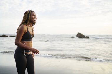 Spor üst modern kulaklıklar en sevdiğiniz müzik şarkıları dinleme giyinmiş neşeli Afrikalı kadın koşucu tropikal adanın deniz kıyışeridi, sağlıklı yaşam tarzı kavramı üzerinde spor egzersiz yürüyüş sırasında