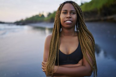 Spor sabah antrenmanı sonrası sahilde duran koyu tenli ve serin korkuları ile motive genç kadın, afro-amerikan kadın koşucu eşofman giymiş uzağa bakarak ve egzersiz için zaman zevk