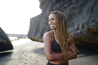 Neşeli koyu tenli sportwoman aktif giysiler kayalar yakınında gülümseyen giymiş, heyecansportif afro amerikan genç kız zayıflama için sabah kardiyo egzersiz önce açık havada şık üst ayakta