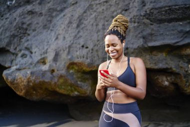 Mutlu koyu tenli kadın jogger sabah egzersiz açık havada radyoda serin müzik mutlu, neşeli heyecanlı kadın eğitim öncesi hücresel bağlı kulaklık çalardan ses dinleme