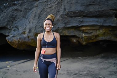 Kulaklıklı müzik uygulamasından ses şarkıları dinlerken kameraya gülümseyen mutlu afro amerikalı genç kadının portresi, spor eşofman giymiş neşeli koyu tenli koşucu heyecanlı