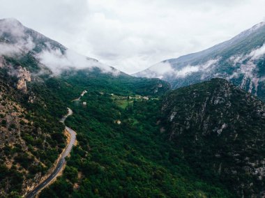 Yağmur sonrası sis ile kaplı yeşil bitki örtüsü ile kayalık dağlarda asfalt yol Pass havadan manzara görünümü. Yukarıda ağır bulutlar asılı pitoresk bisiklet yolu ile kayalık tepeler kuş bakışı görünümü