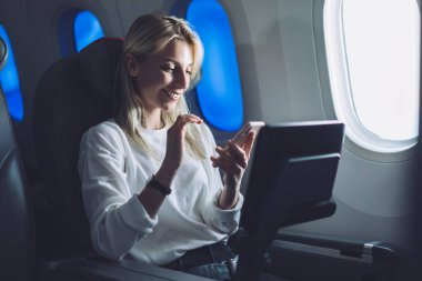 Kablosuz ağ erişimiyle rahat uçuşun tadını çıkarırken cep telefonundan mesaj atan beyaz kadın yolcu. Genç turist kadın internet bağlantısı olan havayolu şirketini seçti