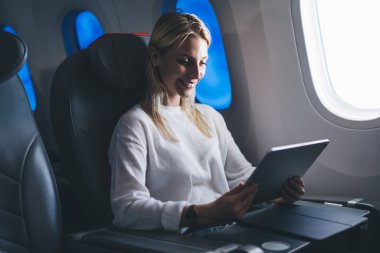 Keyifli uçuşlar ve Wifi internet bağlantısının tadını çıkaran kaygısız bayan yolcunuz kutlu olsun. Kafkasyalı genç kadın havayolu internet sitesi. Gülümseyen blogcu seyahat makalesi okuyor