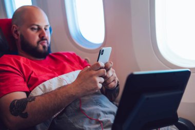 Beyaz erkek yolcu geniş koltukta rahatlıyor ve kablosuz internet erişimi kullanıyor. Genç adam ağ bağlantısı ile First Business Class servisinde rahat uçuşun keyfini çıkarıyor. 