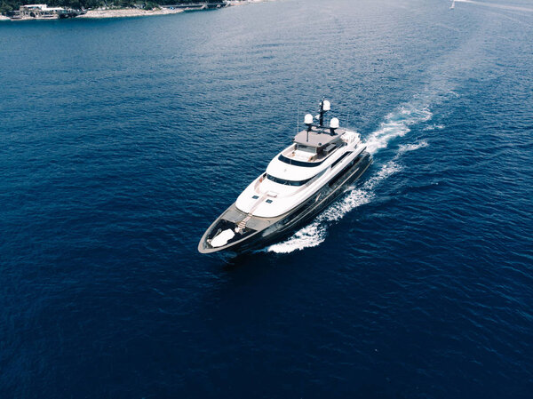 Aerial view of luxury yacht goes to open sea with beautiful blue colour of water. Wealth recreation lifestyle. Bird's eye view of expensive floating ship traveling by Europe in summer