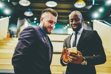 Resmi giyinmiş Afro-Amerikan CEO 'su dostça bir toplantı sırasında internet sitesinde iş ortağına iyi haberler veriyor. Neşeli iki erkek girişimci internetten video izliyorlar.
