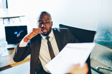 Takım elbiseli dalgın Afrikalı Amerikalı işadamı ofiste çalışırken mali rapor belgelerini bilgiyle kontrol ediyor. Bütçe giderleri olan konsantre erkek girişimci fatura okuyor.