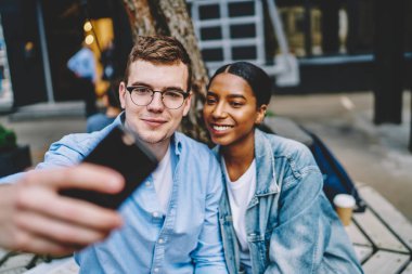Birbirine aşık pozitif çok kültürlü çiftler sosyal ağlar için akıllı telefonlarda selfie çekiyorlar. Neşeli çeşitli arkadaşlar cep telefonlarıyla fotoğraf çekiyorlar.