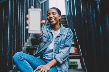 Ağ içeriğine yapıştırıcı reklamı yapmak için akıllı telefon kullanan Afrika kökenli Amerikalı bir kadın. Neşeli ve mutlu koyu tenli blogcu cep telefonunu elinde tutuyor.