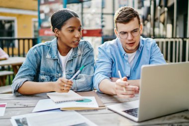 Kafkasyalı zeki bir beyaz, Afrikalı Amerikalı meslektaşına kafenin dışında dizüstü bilgisayarda ilginç bir webinar gösteriyor. Yetenekli genç iş arkadaşları netbook ve Appcatio kullanarak iş birliği yapıyorlar.