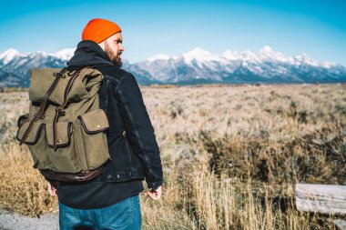 Sırt çantalı, ciddi bir beyaz erkek turist hafta sonunu Alpler 'deki dağların tepesine çıkmak için harcıyor. Genç adam, yüksekliğe giden en iyi rotalara odaklanmış ve çevreye bakıyor.