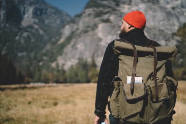 Sırt çantasıyla gezen genç turistin, dağların güzelliğinin tadını çıkaran tecrübeli erkek yürüyüşçünün Park 'taki vahşi toprakları keşfetmek için zaman harcarken doğal manzara manzarasına baktığı sahne.
