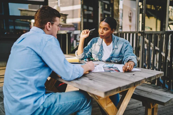 Young multiracial male and female colleagues having conversation about common project at cafe outdoors, confident businesswoman having meeting with man partner for finance consultancy of projec