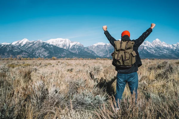 Male traveler with backpack standing with raised hands feeling freedom of life in nature environment, accomplished man enjoying breath of fresh clean air during spring trip to National Park