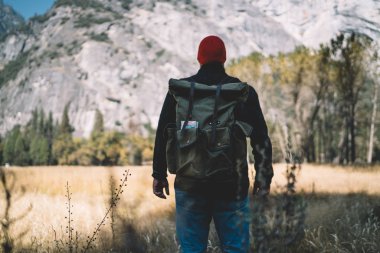 Aktif giyinmiş genç bir adam dağın yamacında dikiliyor ve doğanın güzel manzarasına hayran kalıyor. Tecrübeli bir erkek turist bahar tatili boyunca harika tepelerden keyif alıyor.