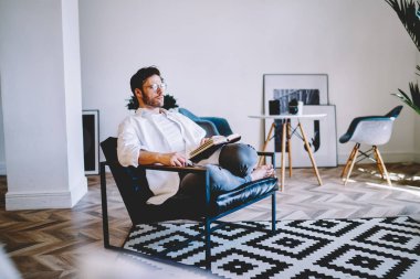 Düşünceli, beyaz tenli bir hippi, evinde rahat bir sandalyede oturuyor ve elinde kağıt defteriyle elinde bir dairede dinlenen çok satan, düşünceli bir gencin entrikalarını düşünüyor.