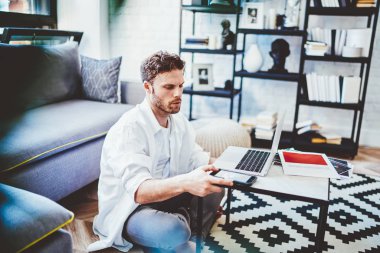 Milenyum çağındaki hippi adam uzaktan kumandalı cep telefonu uyarısını kontrol ediyor. Ev içinde yeni bir dizüstü bilgisayarla çalışıyor. Teknoloji ve iletişim kavramı.