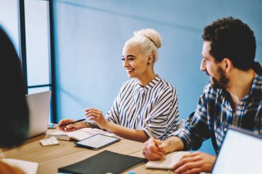 Genç erkek ve bayan meslektaşlar, birlikte çalışma alanında dizüstü bilgisayarlarla masalarda oturup iş kurma planları ve stratejilerini tartışarak işbirliği ve verimli bir toplantıyla tatmin olurlar.