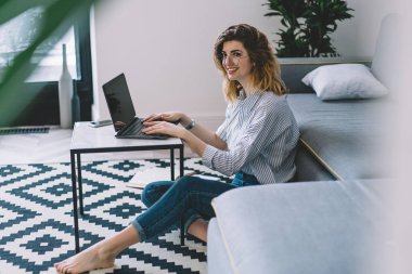 Modern dizüstü bilgisayarın uzaktan kumandasında, şık bir dairede ev internet bağlantısını kullanarak gülen olumlu genç bir kadın. Dairede oturmuş Netbook 'ta ders çalışan hippi kız.