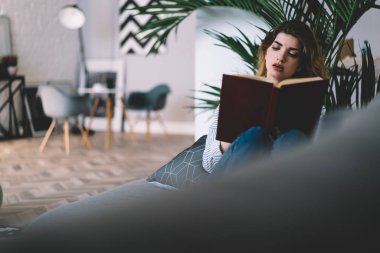 Modern apartman dairesinde ilginç ders kitapları okuyan konsantre genç bir kadın. Düşünceli hippi kız kendi evinde kanepede uzanmış kitaptan bilgi öğreniyor.