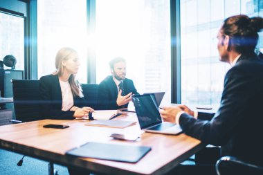 Şirketin iş adamları konferans odasında beyin fırtınası sırasında şirketin finansal stratejisi hakkında işbirliği yapıyor, üç çalışan masaüstünde oturmuş fikirleri tartışıyor ve iletişim kuruyor.