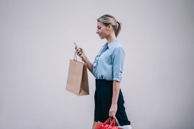 Kafkasyalı, kağıt torbalarla alışveriş yapan, Kara Cuma satışları sırasında alışveriş merkezlerinde akıllı telefon cihazlarıyla internetten alışveriş yapan, tanıtım duvarının yanında yürüyen kadınlar.