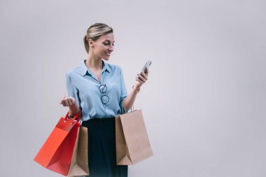 Tarz sahibi beyaz alışverişçiler ellerinde kağıt torbalarla akıllı telefon uygulamalarıyla internet mesajlaşmalarının keyfini çıkarıyorlar. Reklam alanının yakınlarındaki mutlu hipster kız sohbetleri.