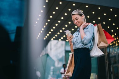 Elinde kese kağıtları olan şık bir kadın alışveriş merkezinin yakınında vakit geçirir ve akıllı telefon cihazından gelen mesajları okur. Cep telefonunda paket numarası olan mutlu hippi kız müşteri.