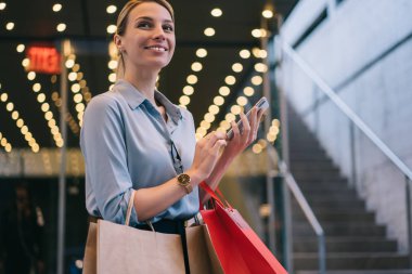 Alışveriş çantaları ve akıllı telefonları elinde tutan ve Kara Cuma boyunca gözlerini kaçıran neşeli bir kadın. Çekici gülümseyen hippi kız boş zamanlarında reklam alanında beklerken telefon bekliyor.