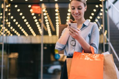 Elinde alışveriş paketleriyle gezen neşeli yeniyetme kız çevrimiçi müşteri hizmetleriyle akıllı telefon mesajlarının tadını çıkarıyor. Günlük kıyafetleri olan pozitif kadın cep telefonu satışlarında 4G 'ye bağlı.