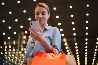 Tüketim ve gençlik yaşam tarzı konsepti, renkli alışveriş çantaları tutan pozitif genç kadın ve Kara Cuma boyunca favori mağazalarda satış ve fiyatları kontrol etmek için modern akıllı telefon cihazı