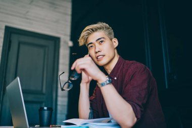 Çinli bir erkek öğrencinin bilgisayar başında modern bir aletle bilgisayarla çalışırken düşünceli davranması, Japon hipster adamın üniversite projesi hakkında düşünmesi.