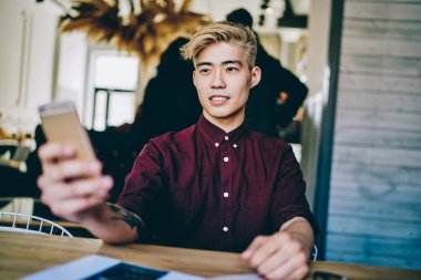 Japon hipster adam elinde cep telefonuyla tanıtım alanına bakıyor ve Çin 'li erkek blogcunun elinde modern akıllı telefon ile kablosuz bağlantısını bekliyor.