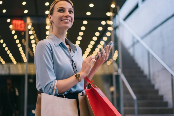Glada Kvinna Som Håller Shoppingväskor Och Smartphone Händerna Och Tittar — Stockfoto