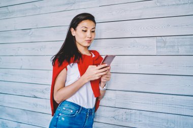Reklam metinleri için fotokopi alanının yanında duran çekici Asyalı hippi kız ve arkadaşlarıyla çevrimiçi sohbet için modern cep telefonu kullanıyor.