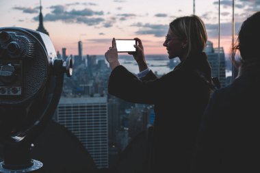 Dişi turist akıllı telefon kamerasını New York manzarasını, açık gözlem güvertesinden çekmek için hazırlıyor. ABD tatilinde cep telefonu şehir simgesinde fotoğraf çeken hippi kız.
