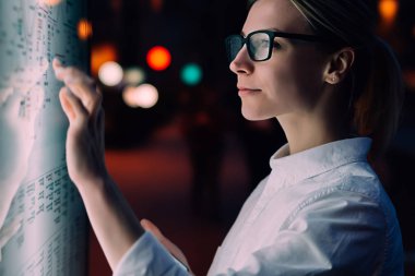 Toplu taşımacılık metro haritası ile etkileşimli kiosk. Akıllı telefon ile büyük ekranda duran kadın. Cep telefonunda tren tarifesi uygulaması kullanırken parmak ekranı ile dokunan genç kadın.