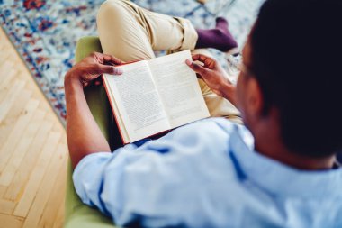 Afro-Amerikan hipster 'ın açık bir kitap tutarken çekilmiş görüntüsü. Ev içinde boş zaman geçiriyor. Koyu tenli bir adamın ilginç edebiyat kitapları okuduğunu görüyor.