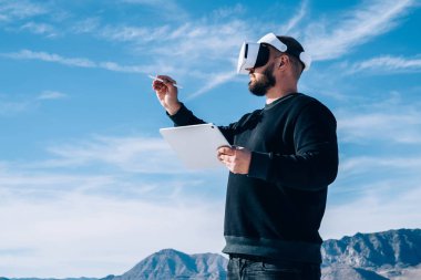 Erkek milenyum mimarı yeni şehrin yapısını tablet ve sanal gerçeklik kulaklığı kullanarak elektronik çizimler yaparak tasarlıyor. Yenilikçi teknoloji, erkek dijital kalemle VR dünyasına dokunuyor