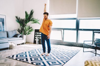 Genç adam, modern odada şık bir halı üzerinde sabah egzersizi yaparken el ele tutuşup ısınıyor. Evdeki antreman sırasında yoga yapan hippi çocuk sağlıklı bir yaşam tarzı sürdürüyor.