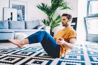 Genç adam evde sağlıklı yaşam tarzını ve spor vücut şeklini destekleyen yoga egzersizleri yapıyor. Kaliteli iç dekorasyonla birlikte. Hippi adam sabah antrenmanı sırasında düz alanda meditasyon yapıyor.