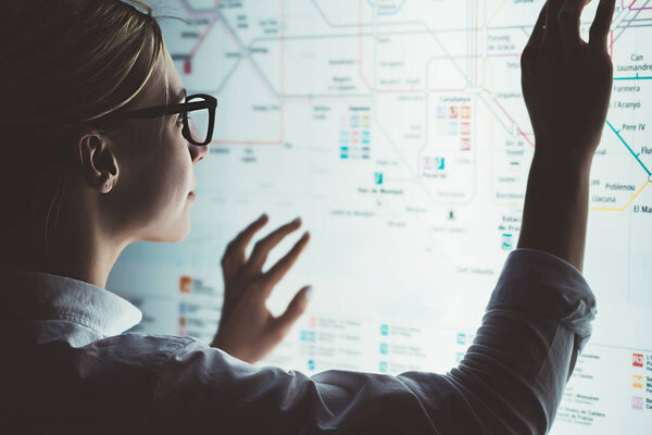 Digital monitor with public transport subway map. Female standing at big display with advanced innovative technology. Young woman touching with finger sensitive screen while selecting surface option