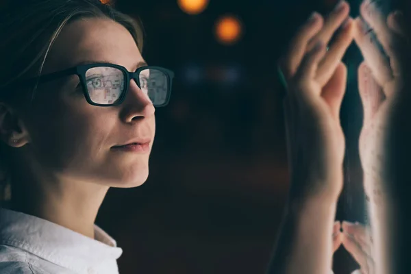 先進的な革新的な技術でディスプレイに立つ女性 表面オプションを選択しながら 指の敏感な画面で触れる若い女性 夜の光が顔に反映されたインタラクティブなキオスク — ストック写真