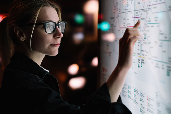 Digital monitor with public transport subway map. Female standing at big display with advanced innovative technology. Young woman touching with finger sensitive screen while selecting surface option