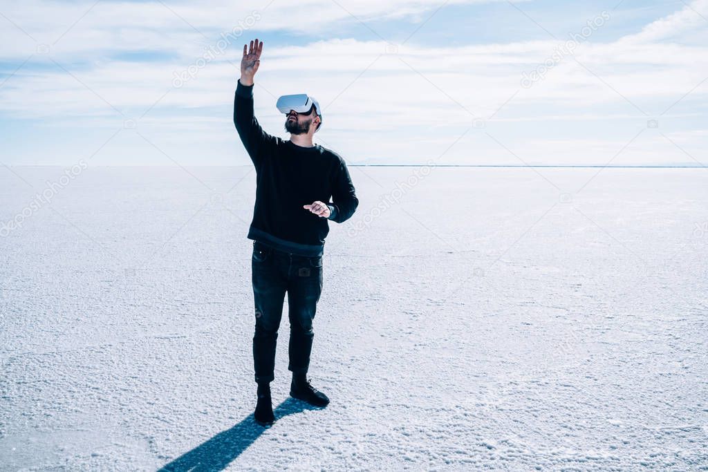 Man in virtual reality headset gesturing with hands to control simulation of 3D futuristic dimension while standing outdoors in empty nature space.Hipster guy touching something in augmented VR world